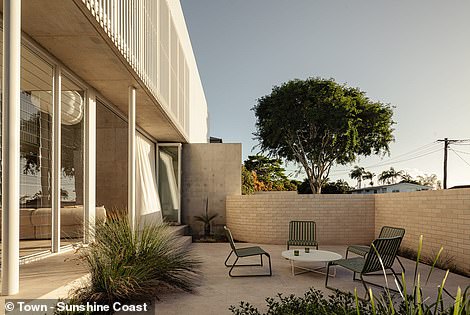 A sun-drenched patio with grass trees sits on one side of the living room and an outdoor patio leading to the leafy backyard sits on the other.