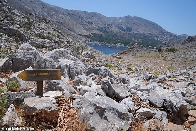 A direction sign pointing towards Agia Marina on a rocky road in the Pedi Hills (Pedi center in the distance, right), a small fishing village