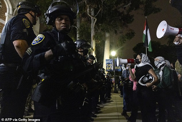 Police line up against organized protesters shouting at them through loudspeakers