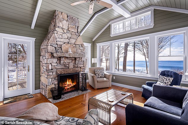 In the living room, a large stone fireplace is surrounded by abundant natural light, exposed ceiling beams, and beautiful hardwood floors.