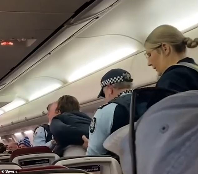 Officers removed the man from his seat (pictured) after he refused to get up, before being escorted off the plane as dozens of shocked passengers looked on.