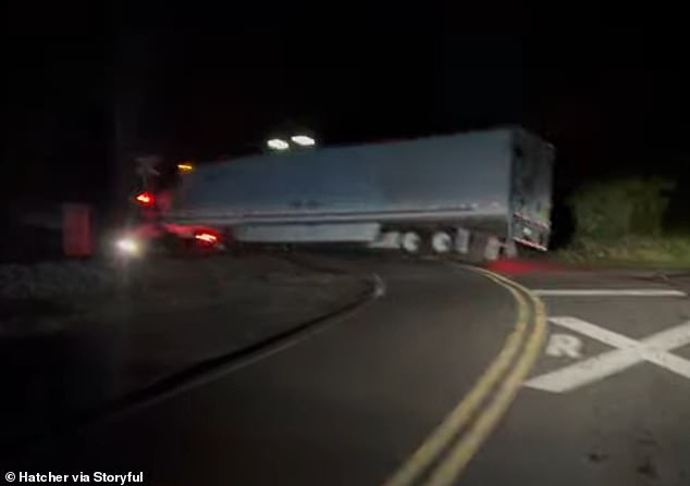 In the images, the trapped truck is on both sides of the train tracks. It's night and the railroad crossing signal is flashing red.