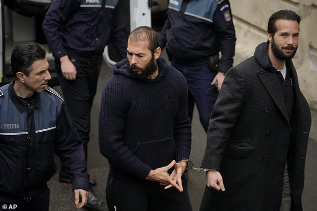 Tate (center) handcuffs his brother Tristan as he arrives at the Court of Appeal in Bucharest, Romania, in February 2023. The sign is to help him 