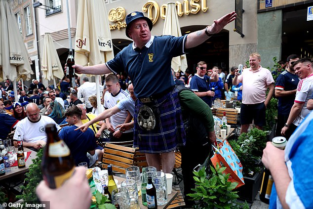 A kilt-clad Scottish fan stands on a chair and leads the chants while holding a bottle of beer.