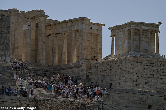 Tourists sit on the stairs of the ancient Acropolis hill during a hot day in Athens, Greece