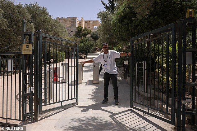 An employee closes the exit gate of the Acropolis Hill archaeological site, which is temporarily closed due to a heat wave sweeping the country.