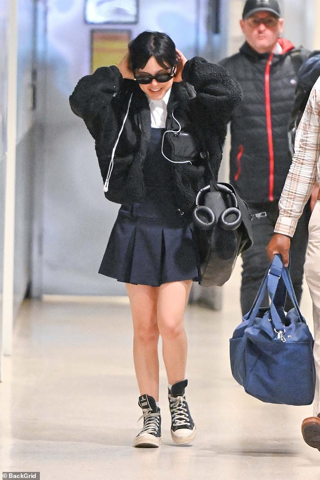 The Scream alum, 21, was photographed smiling from ear to ear after landing while carrying a large black bag with her.