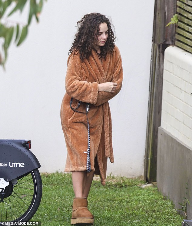 The reality star stayed warm in a brown robe and Ugg boots as she watched her two dogs sitting on the grass.