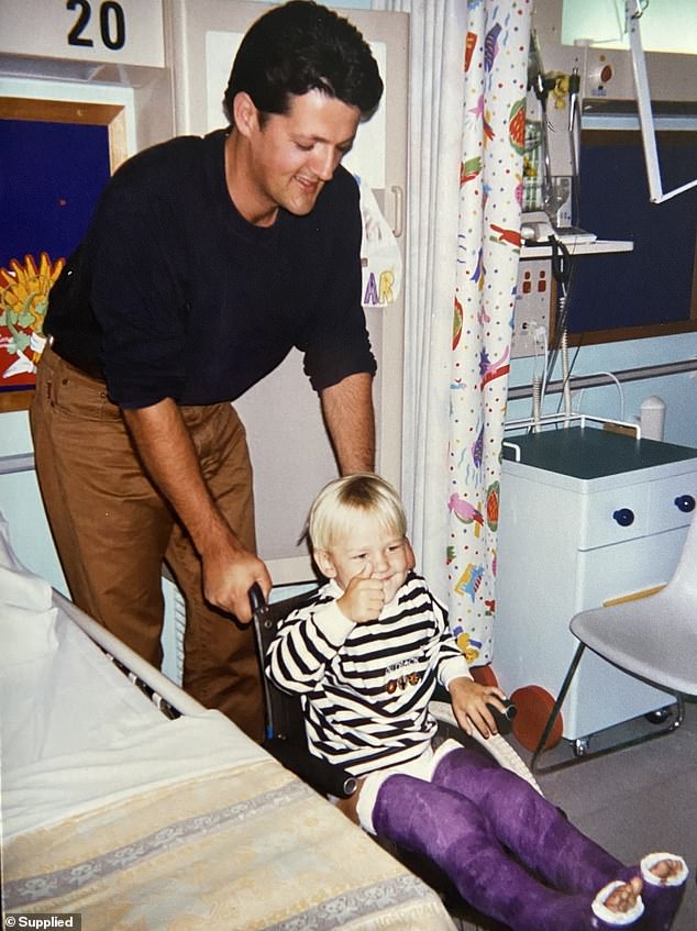 Three-year-old Oscar is seen giving a thumbs up as his father pushes his wheelchair.