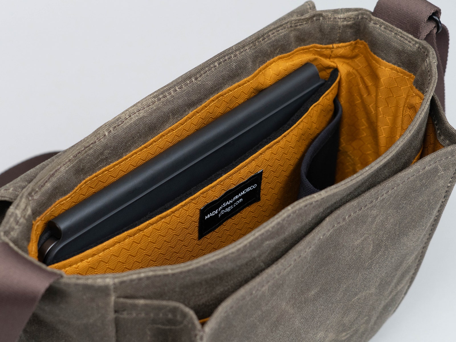 Top view of a cloth bag with the front flap facing back showing the orange interior and a pocket with a tablet