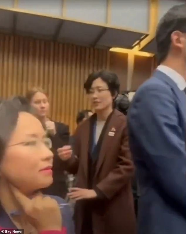 Cheng Lei (left) is seen with a Chinese official nearby trying to block his view.