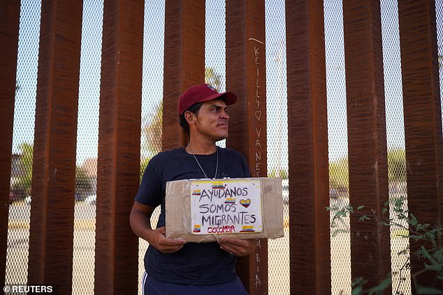 Colombian migrant David Laguada holds a banner reading "Help us we are migrants" while waiting with his family for a CBP One appointment to reach the United States next to the border wall during a heat wave in Mexicali, Mexico.