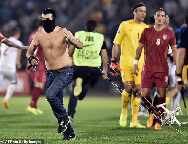 A masked Serbian supporter flees with the drone carrying the controversial flag as players watch in the background.