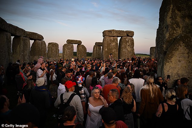 Hundreds of people gather inside the stones, including families with small children on their shoulders.