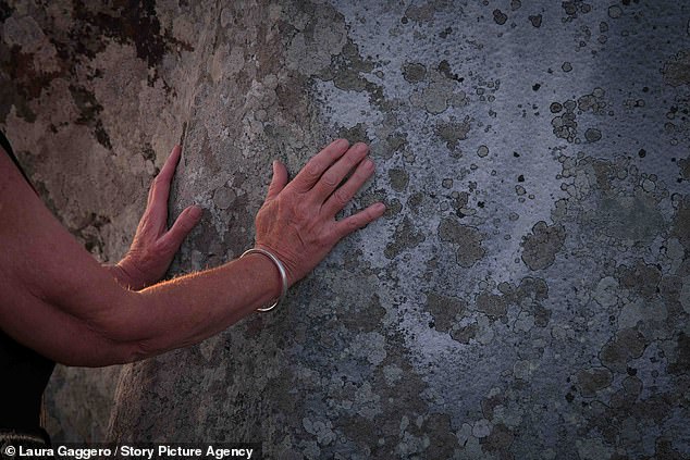 A woman puts her hand on ancient rocks Thursday afternoon