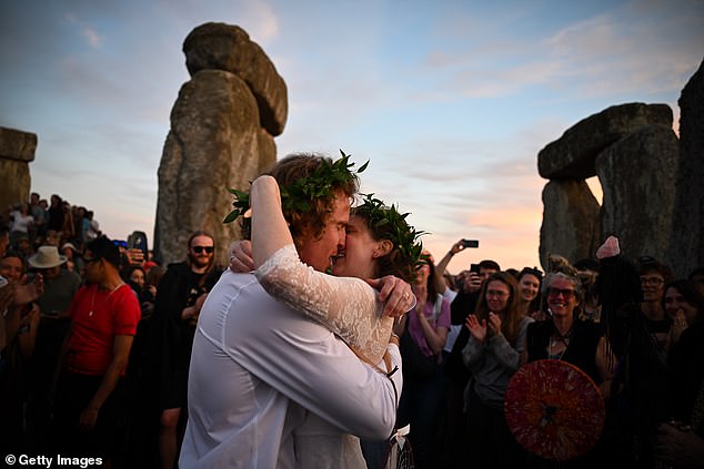 The married couple kisses while others applaud and take photos.