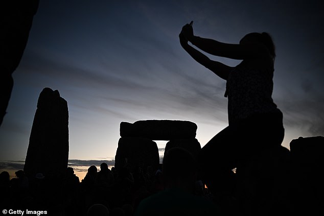 A woman takes a photo sitting on a friend's shoulders at Stonehenge.