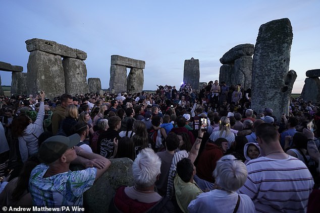 People gather at sunset at Stonehenge in Wiltshire, as they wait to welcome the summer solstice.