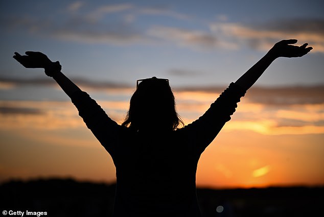 A woman raises her arms as the sun sets at Stonehenge.