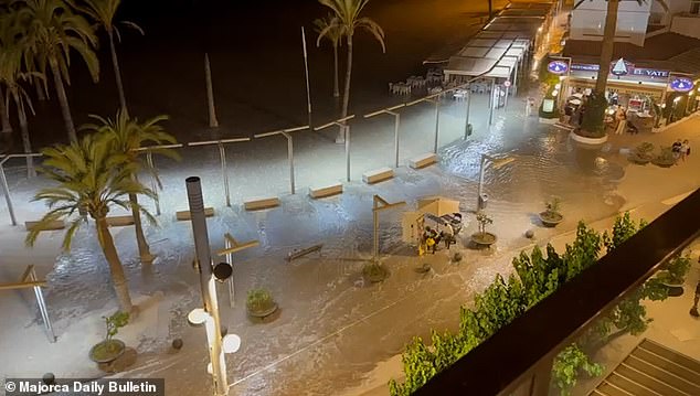 Chairs are seen submerged in the water after the storm surge in Mallorca, with people walking nearby