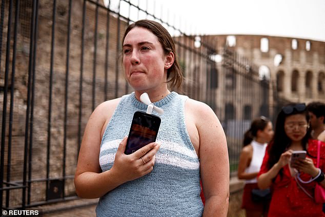 Claira from Massachusetts uses a fan connected to her iPhone to cool herself while waiting in line to enter the Roman Forum