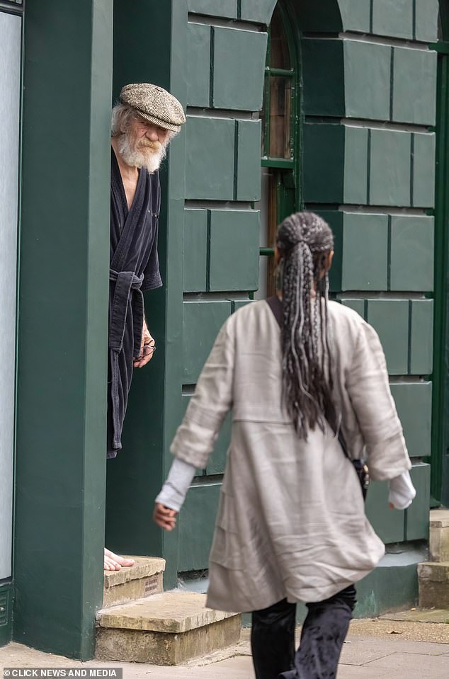 A woman walks past as Sir Ian McKellen looks on from his home in London yesterday.