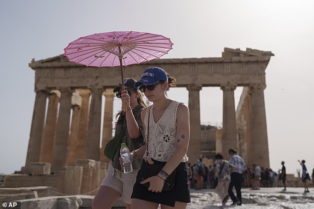 Tourists with umbrellas walk in front of the Parthenon on the ancient Acropolis in central Athens, Wednesday, June 12, 2024.