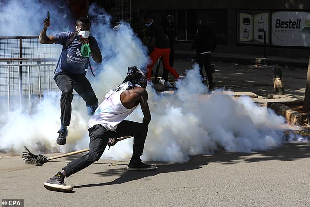 A protester uses a broom to repel a tear gas canister