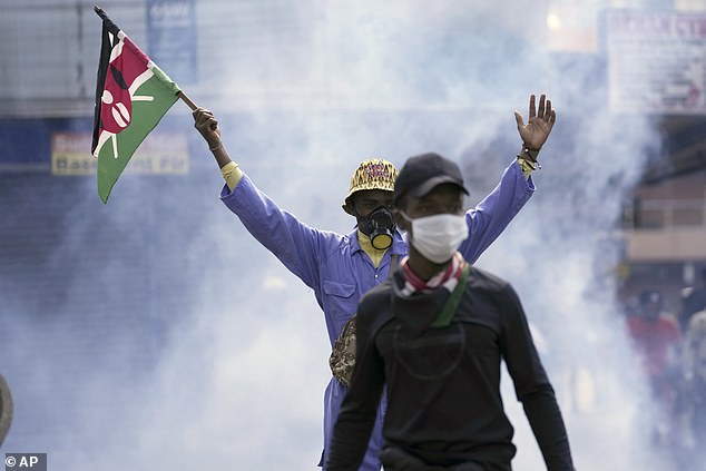 An anti-government protester waves a Kenyan flag as police fire tear gas at them.