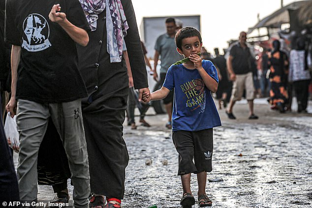 A boy eats a slice of watermelon as he walks with a woman along a market street in Deir el-Balah, central Gaza Strip, June 27, 2024.