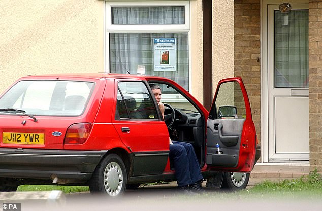 Ian Huntley sits in his car outside his home in Soham, Cambs, as his then girlfriend Maxine Carr displays a poster of missing schoolgirls (file image)