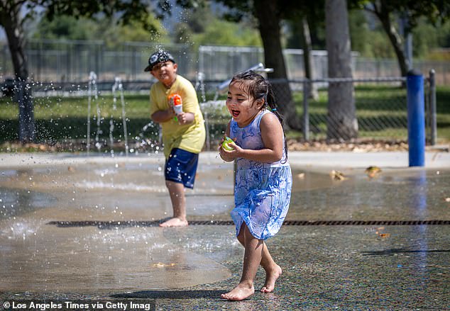 A four-year-old girl runs through a spray pool to cool off as another child sprays her in the heat at Rio de Los Angeles State Park in Los Angeles.