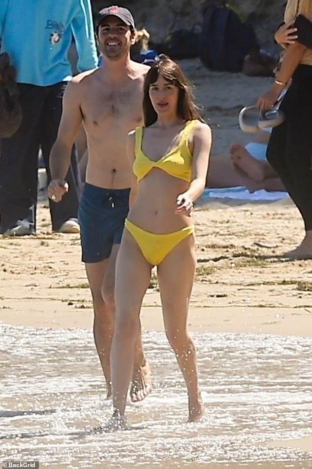 Dakota, who is godmother to Ezer and Dolores, flaunted her incredible physique as she walked across the sand in a fun yellow bikini.