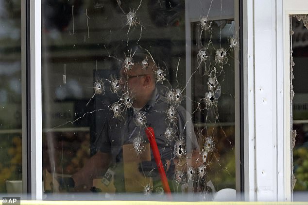 Damage can be seen on a front window. Law enforcement officers work at the scene on Friday.