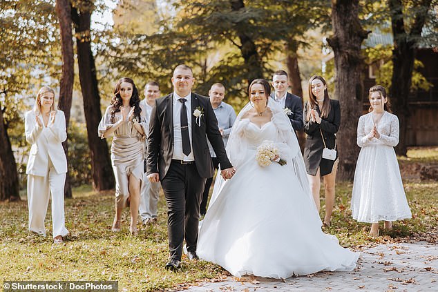 A bride and groom walk along a path with a group of people behind them, dressed in white (file image)