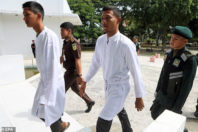 Two of the men in white robes are seen arriving at the building in Banda Aceh where they were flogged late for violating the region's Sharia law on alcohol consumption.