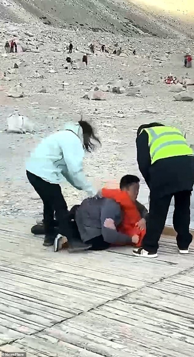 The woman in the light blue coat tries to push one of the men away.