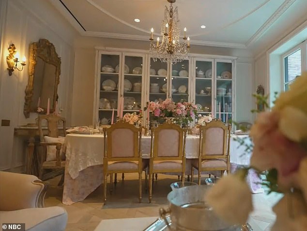 A fabric-covered dining table is flanked by gold chairs, as well as a stunning chandelier and several bouquets of fresh flowers.