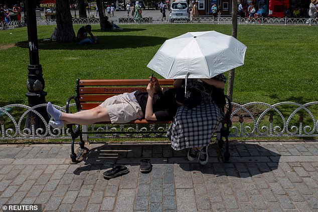 People protect themselves from the sun with an umbrella as they stand at Sultanahmet Square, one of the city's best-known tourist attractions, in Istanbul, Turkey, June 28, 2024.