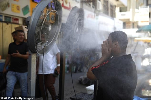 A man cools off as he stands in front of 'water spray fans' placed on the side of the road as temperatures soar in the capital Baghdad on June 30, 2024