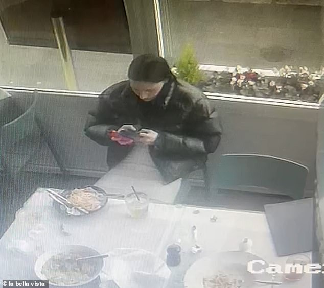 A woman, wearing a white dress and a black quilted jacket, looks at her phone before her quick escape.