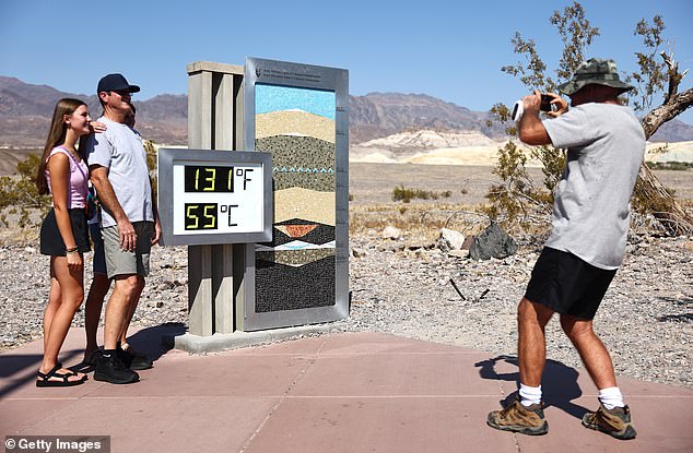 Tourists pose next to an unofficial thermometer in the afternoon heat at the Furnace Creek Visitor Center