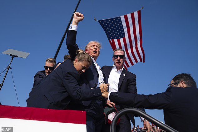 Trump raises his fist toward the crowd as security removes him from the stage after being shot.