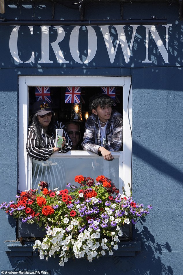 From one crown to another: Islanders peer out of the window of The Ship and Crown pub to take a photo of the King and Queen