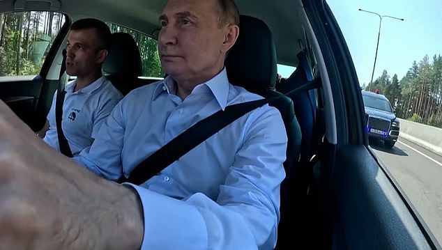 Images taken from inside the vehicle show Putin driving along the highway in a white shirt with the top button undone.