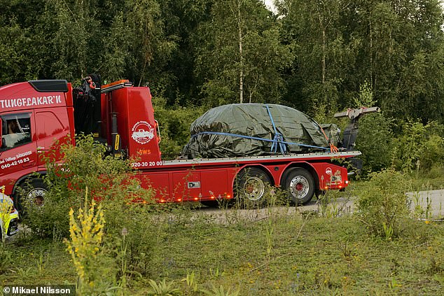 A truck is seen transporting the burnt car which appears to have been wrapped in a plastic sheet.