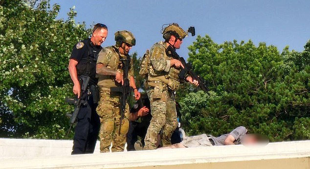 Law enforcement personnel stand over the body of Thomas Matthews Crooks on a rooftop near the Trump rally on Saturday