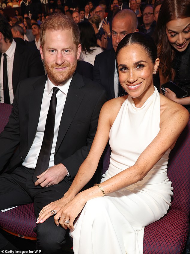 A beaming Meghan Markle places her hand on Harry's leg as the couple pose for the cameras at the glitzy ceremony in Los Angeles.