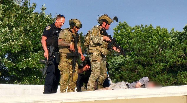 Law enforcement personnel stand over the body of Thomas Matthews Crooks on a rooftop near the Trump rally on Saturday