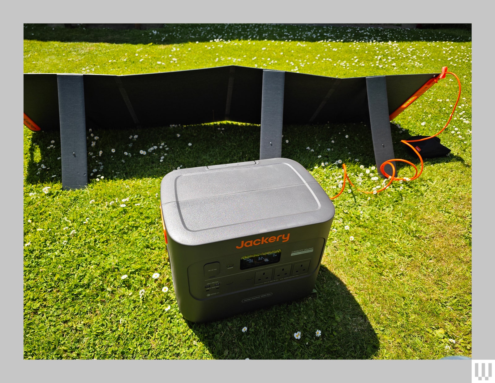 Gray square shaped electrical container attached to braced panels, all sitting on the grass